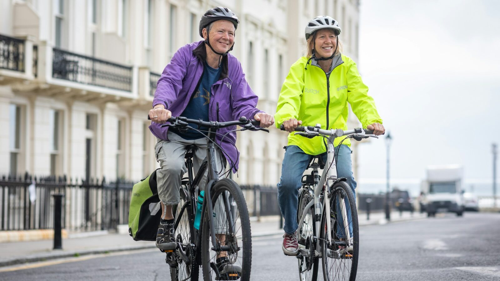 Smiling older couple riding bicycles together in bright jackets on a city street, representing energy and movement after 50.